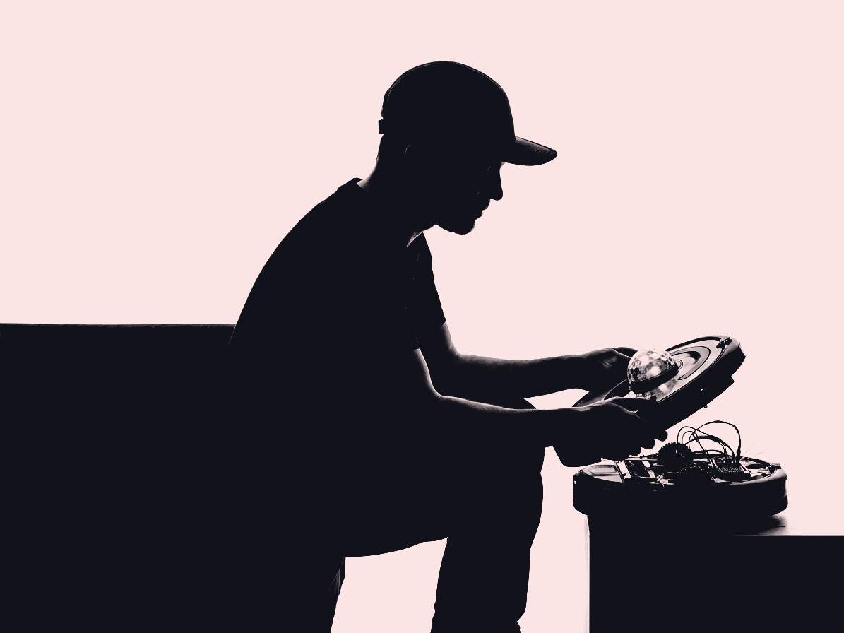 A high-contrast image of a man sitting on the edge of a couch, tinkering with a Roomba