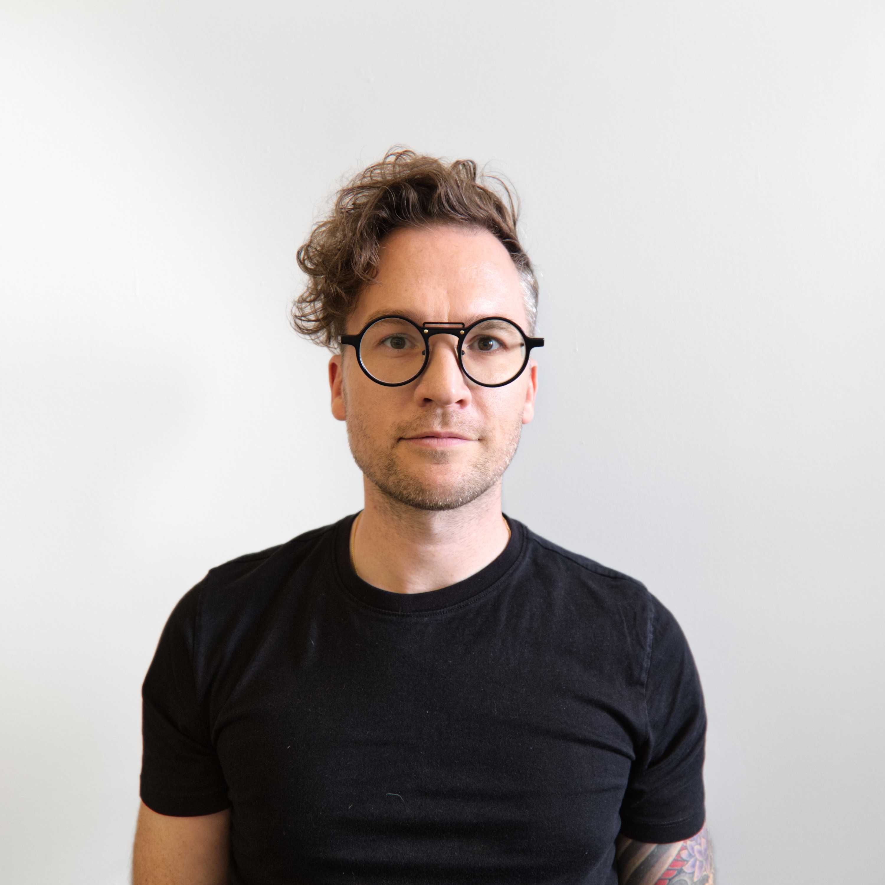 A photo of Shawn wearing round glasses standing against a light grey background