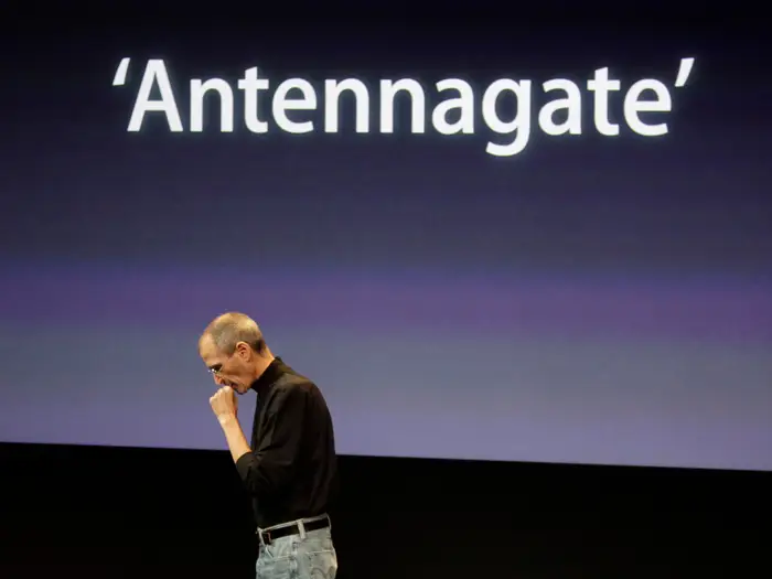 Steve Jobs walking pensively across the stage with the antennagate slide behind him